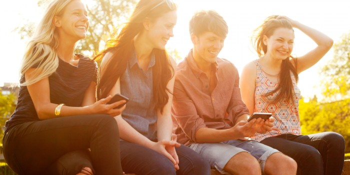 Four friends sat on wall with smart phones.